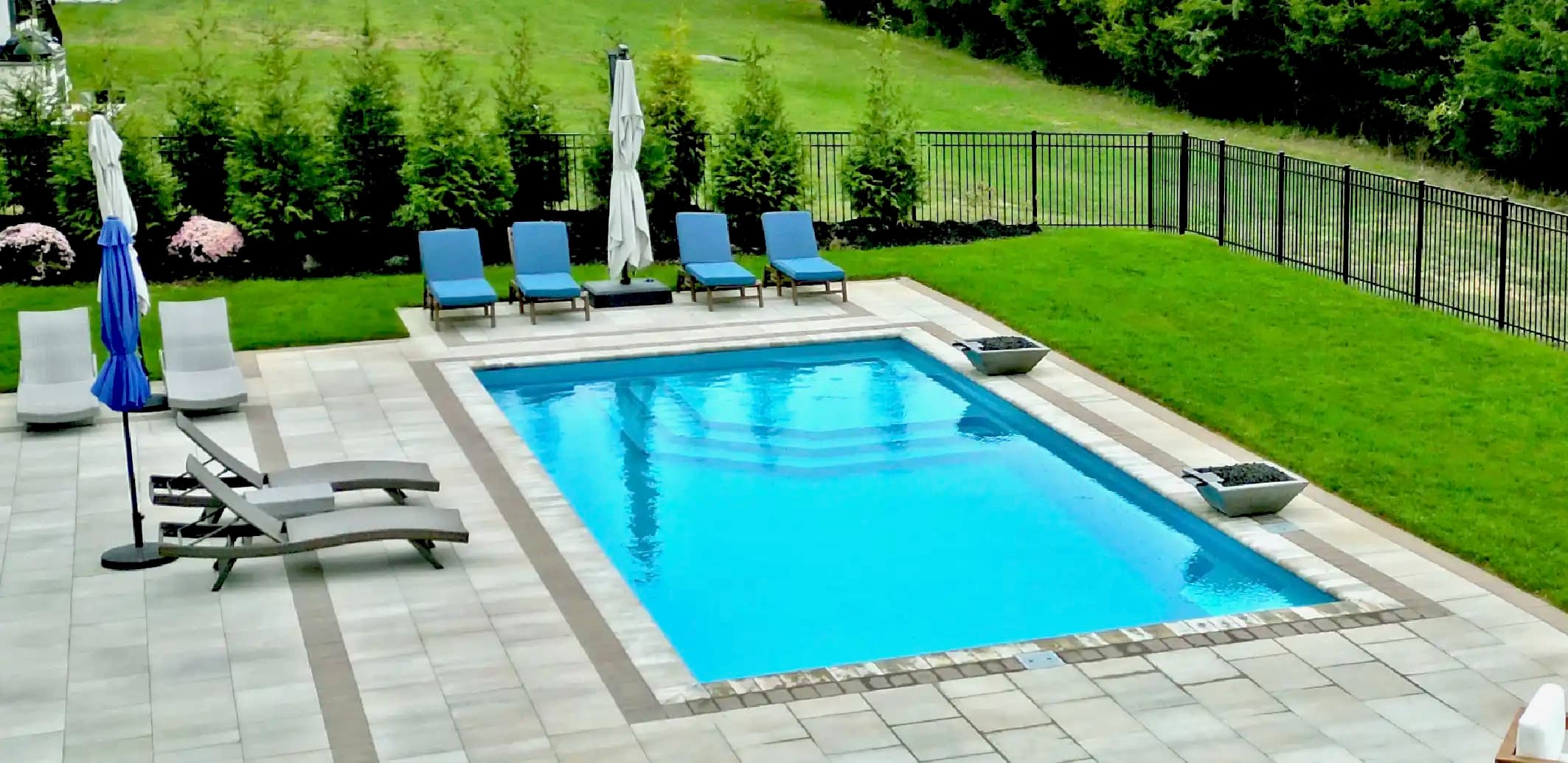 Aviva fiberglass rectangular in-ground pool with paver decking, loungers, and fire bowls
