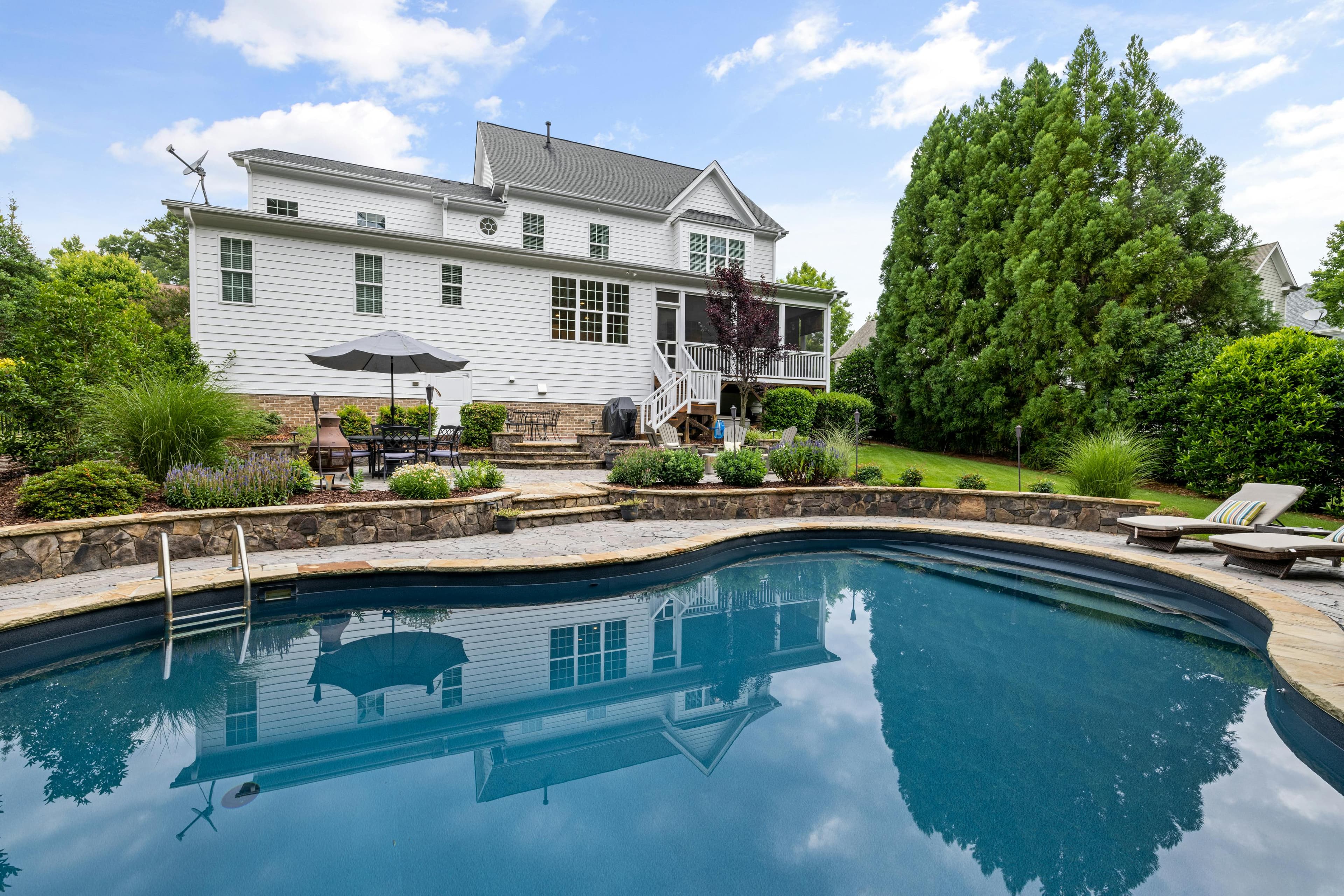 Crystal clear in-ground pool water with sunlight reflections and manicured garden landscaping in the background
