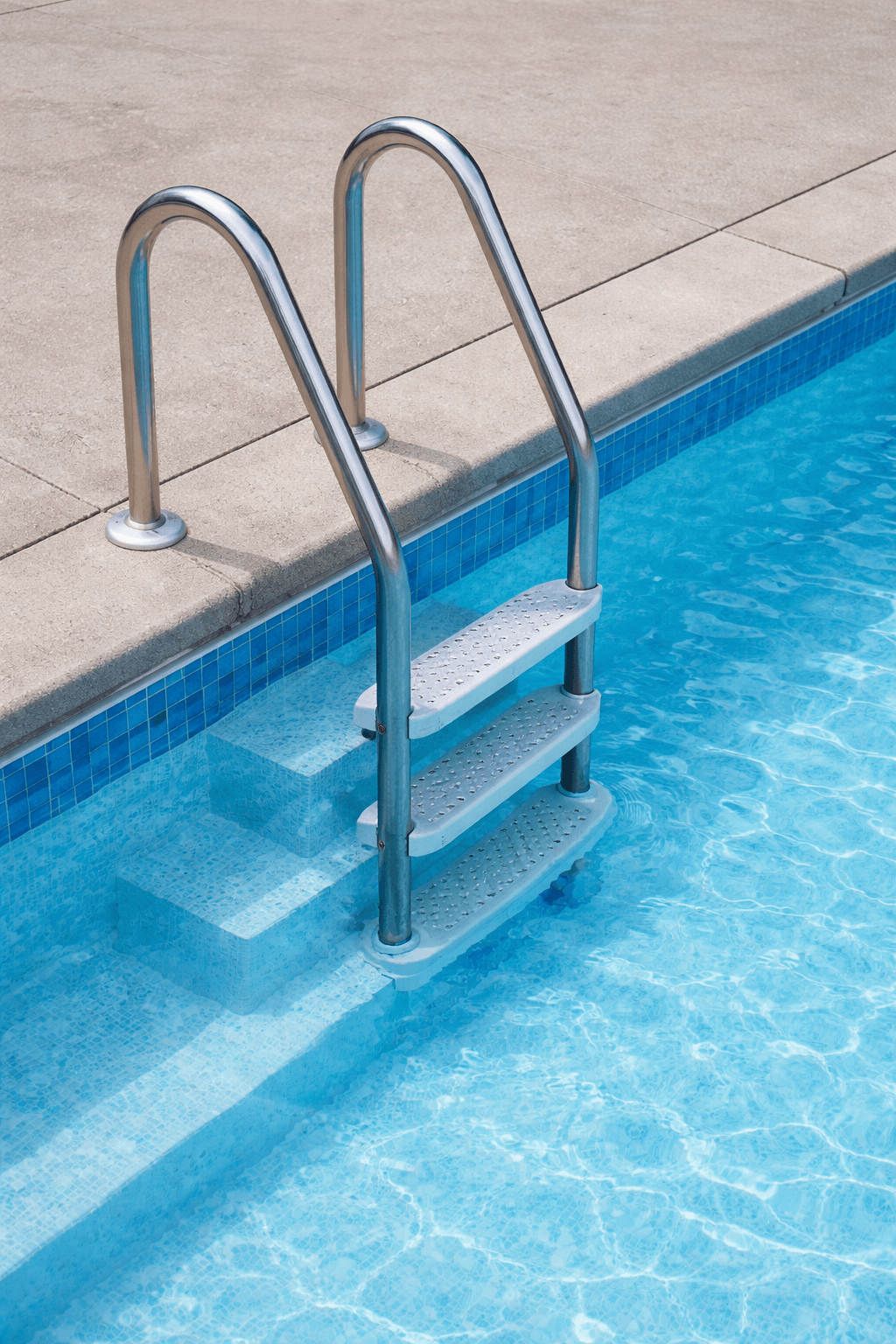 Stainless steel pool ladder entering crystal clear blue pool water with concrete deck edging
